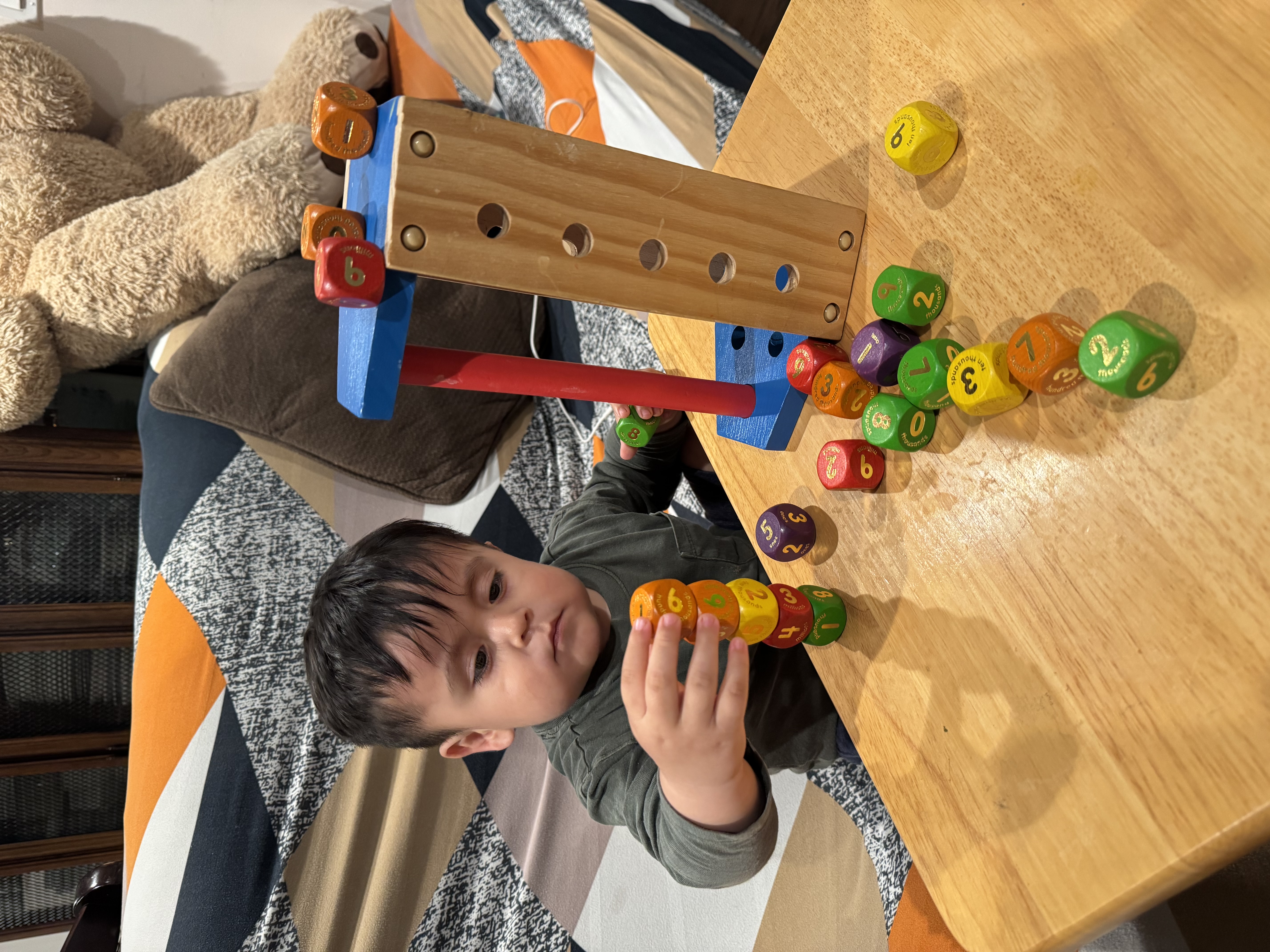 Gael concentrating as he stacks colorful number blocks at a wooden table.